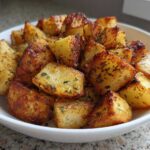 A white bowl filled with golden brown, crispy breakfast potatoes seasoned with herbs.