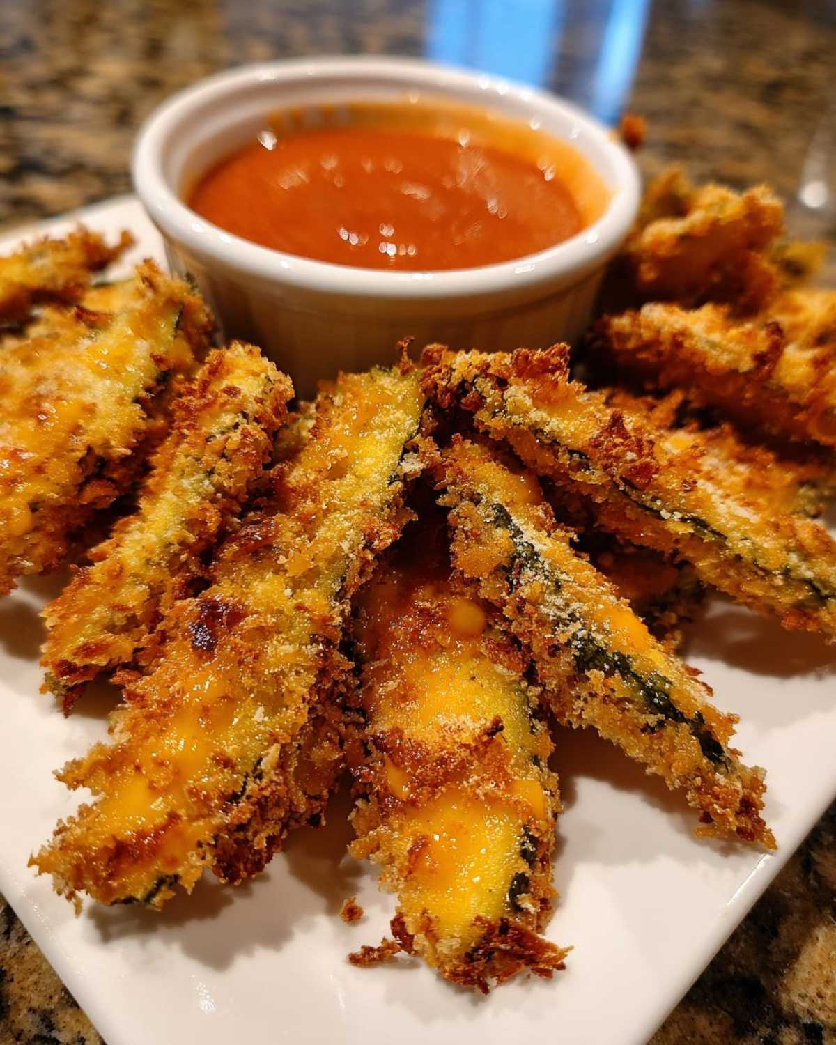 Close-up of golden brown, crispy Fried Pickles served on a white plate with a side of marinara dipping sauce.