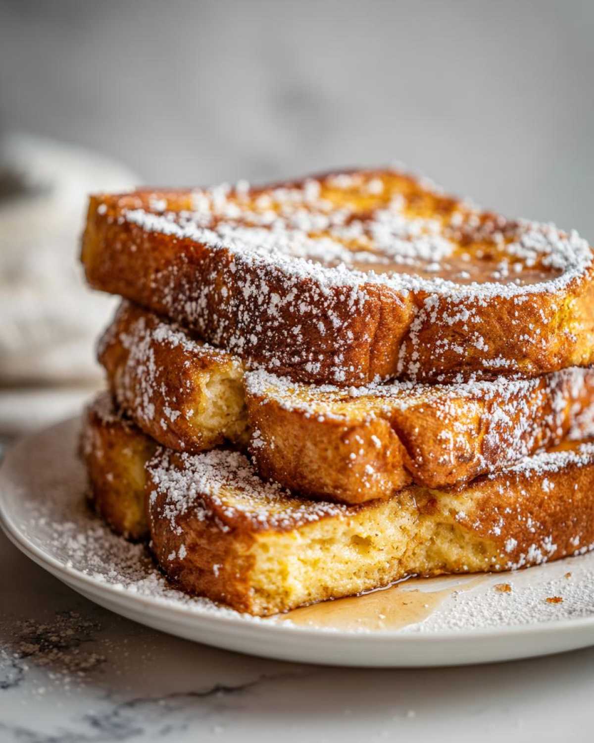 A close-up of a stack of golden brown easy french toast slices dusted heavily with powdered sugar.
