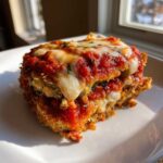 A close-up, appetizing serving of baked eggplant parmesan topped with melted mozzarella and rich tomato sauce.