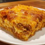 A close-up, featured image of a thick slice of Dorito Casserole with a browned, melted cheese topping.