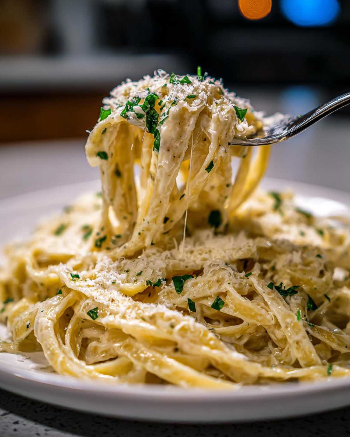 A fork lifting a generous portion of fettuccine coated in creamy Olive Garden Alfredo Sauce, topped with Parmesan and parsley.