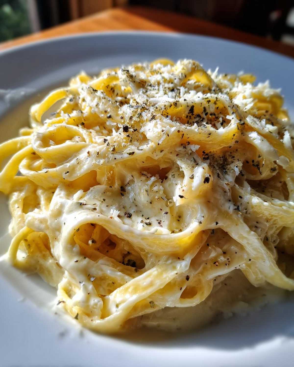 Close-up of fettuccine pasta coated in creamy Olive Garden Alfredo Sauce, topped with Parmesan and herbs.