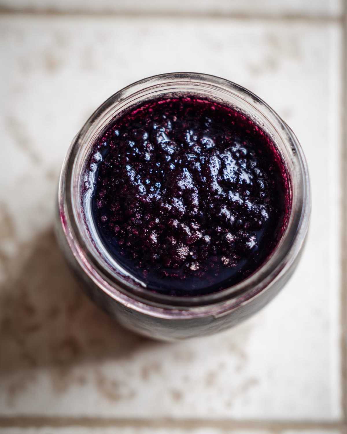 Overhead view of thick, dark purple elderberry syrup recipe inside a clear glass jar.