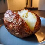Close-up of a crispy-skinned air fryer baked potato, split open to show the fluffy white interior.