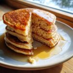 A stack of fluffy almond flour pancakes, cut to show the interior texture, drizzled with maple syrup.