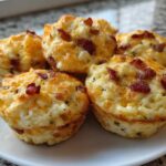 A close-up view of several fluffy bacon and cheese egg bites served on a white plate.