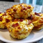 A close-up of several fluffy, golden brown egg bites topped with crispy bacon pieces, ready to eat.