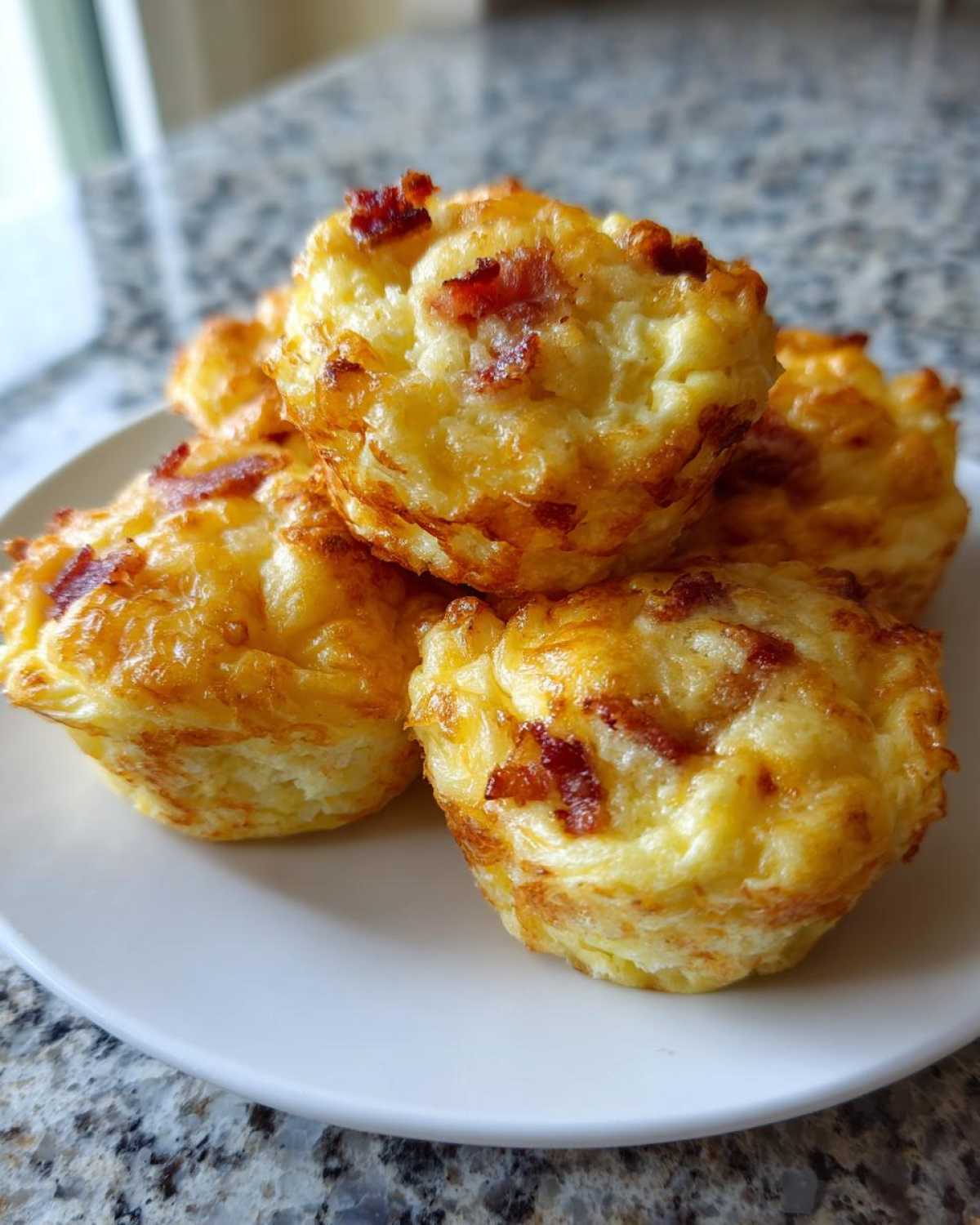 Close-up of fluffy, golden brown bacon egg bites stacked on a white plate, ready to eat.