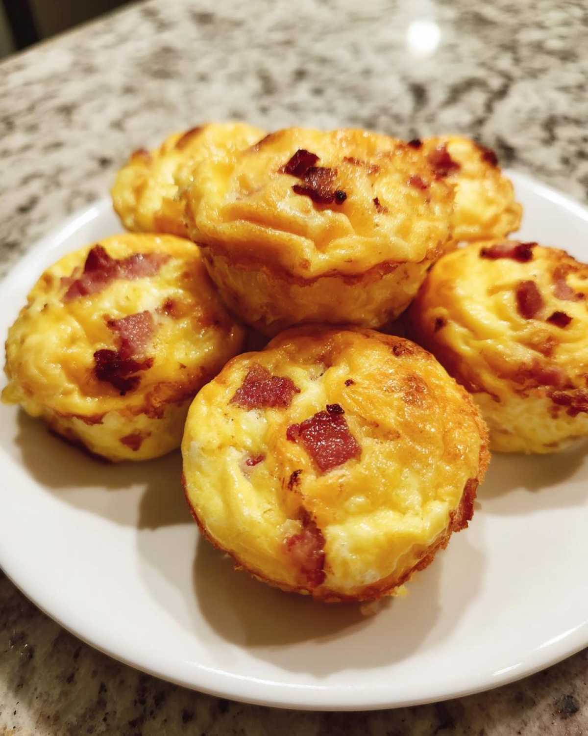 A close-up of several fluffy, golden-brown bacon egg bites stacked on a white plate.