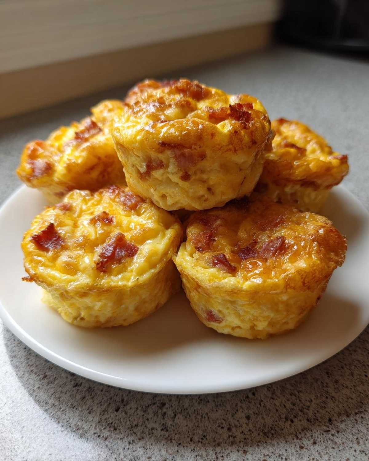 A stack of five fluffy, golden-brown bacon egg bites served on a small white plate.