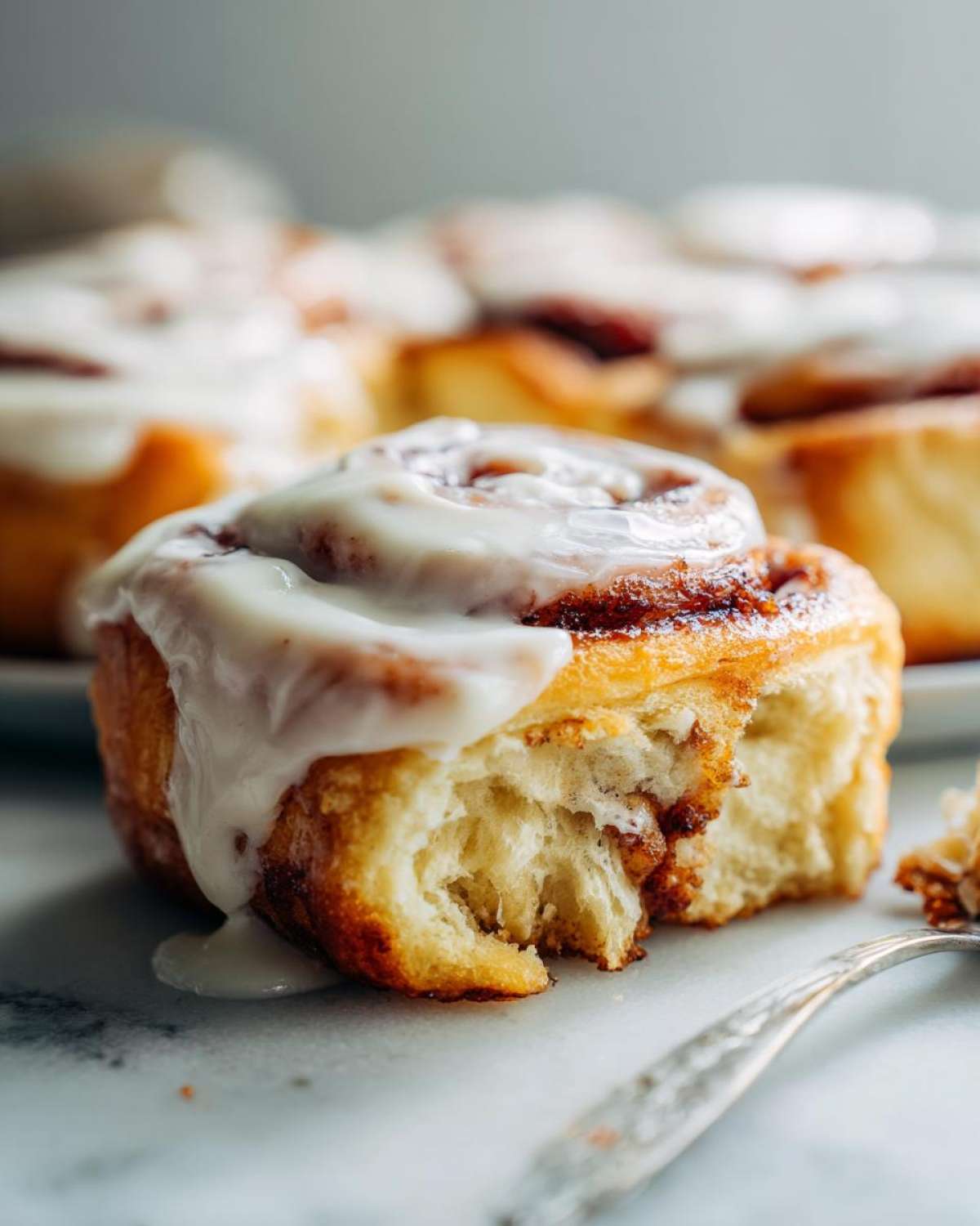 A close-up shot of a soft, fluffy cinnamon roll with thick white icing dripping down the side, showing the interior texture.