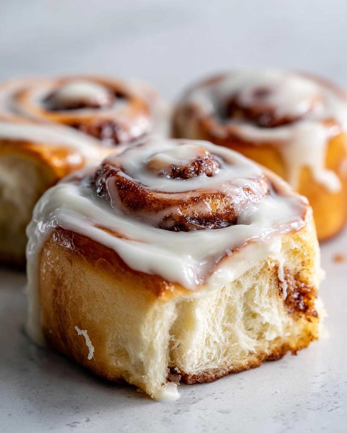 Close-up of a soft, fluffy cinnamon roll with rich cinnamon swirl and thick white icing.