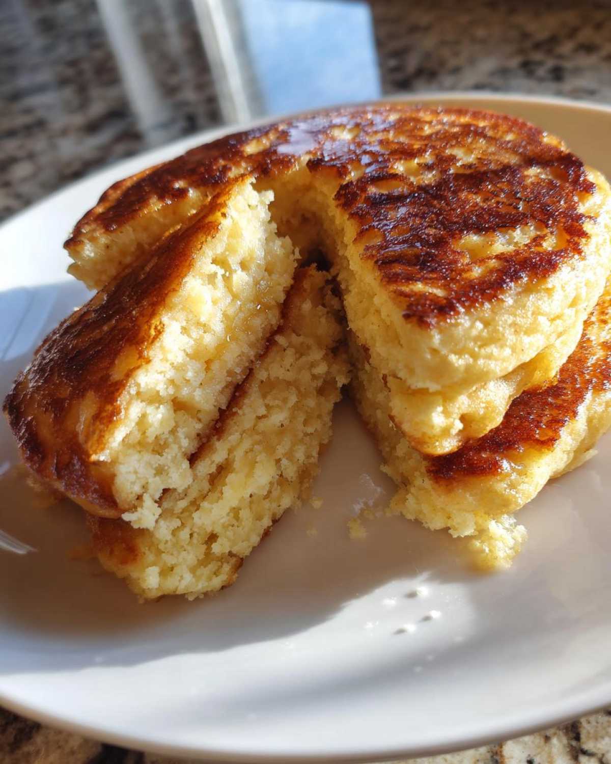 Close-up of fluffy coconut flour pancakes cut open to show the texture, drizzled with syrup.