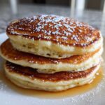 Close-up of a fluffy stack of three greek yogurt pancakes topped with powdered sugar and syrup.