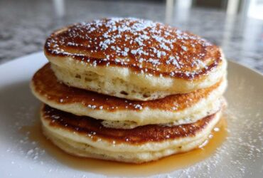 Close-up of a fluffy stack of three greek yogurt pancakes topped with powdered sugar and syrup.