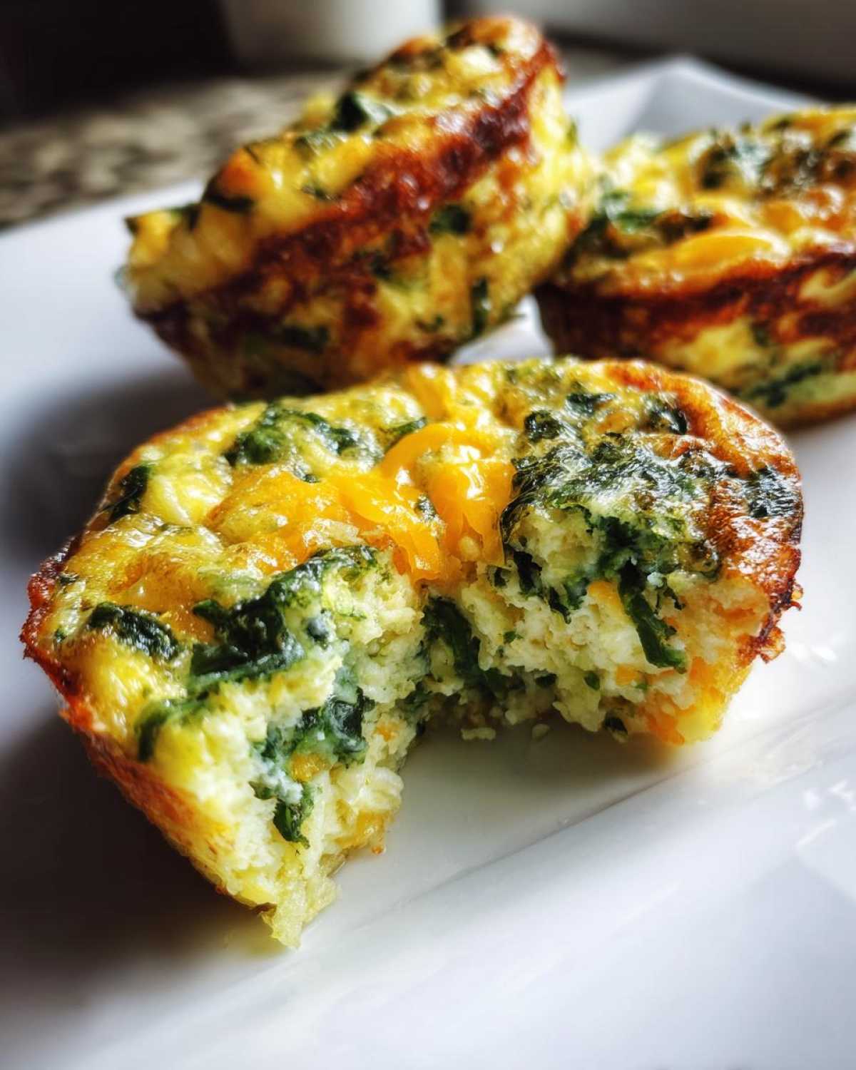 Close-up of a fluffy muffin tin egg bite with a bite taken out, showing spinach and melted cheddar cheese inside.