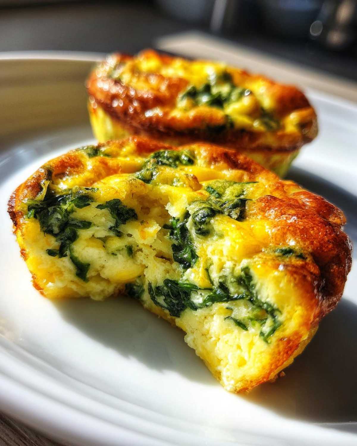 Close-up of a fluffy muffin tin egg bite, bitten into, showing spinach and yellow egg texture.