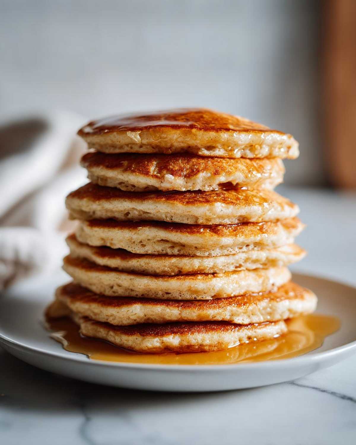 A tall stack of golden brown oatmeal pancakes drizzled generously with maple syrup on a white plate.