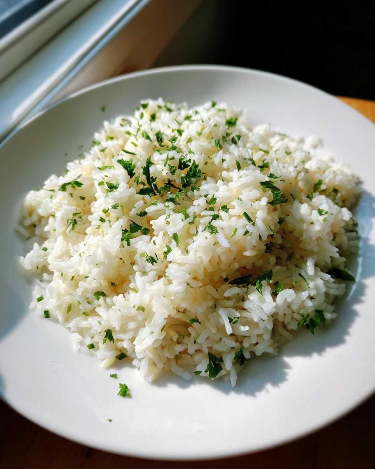 A mound of fluffy white rice pilaf garnished generously with chopped fresh green parsley on a white plate.
