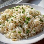A close-up of fluffy rice pilaf garnished with fresh chopped parsley in a white bowl.
