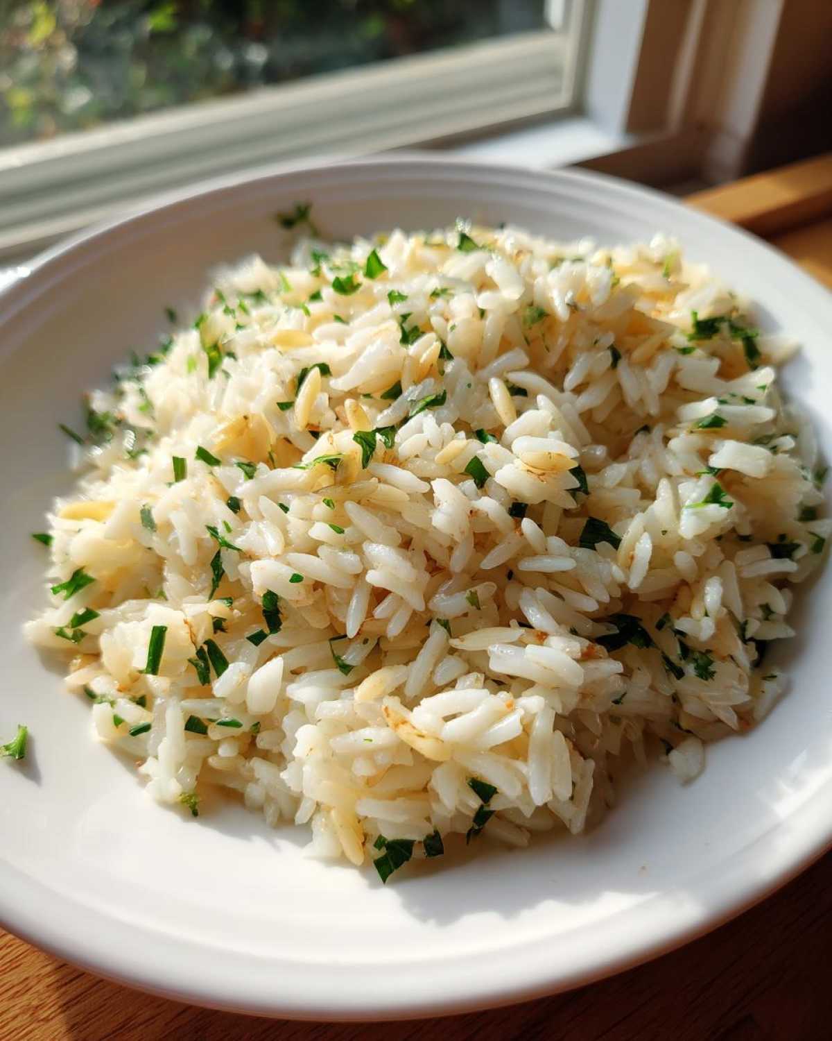 Close-up of fluffy rice pilaf garnished with chopped green parsley in a white bowl.