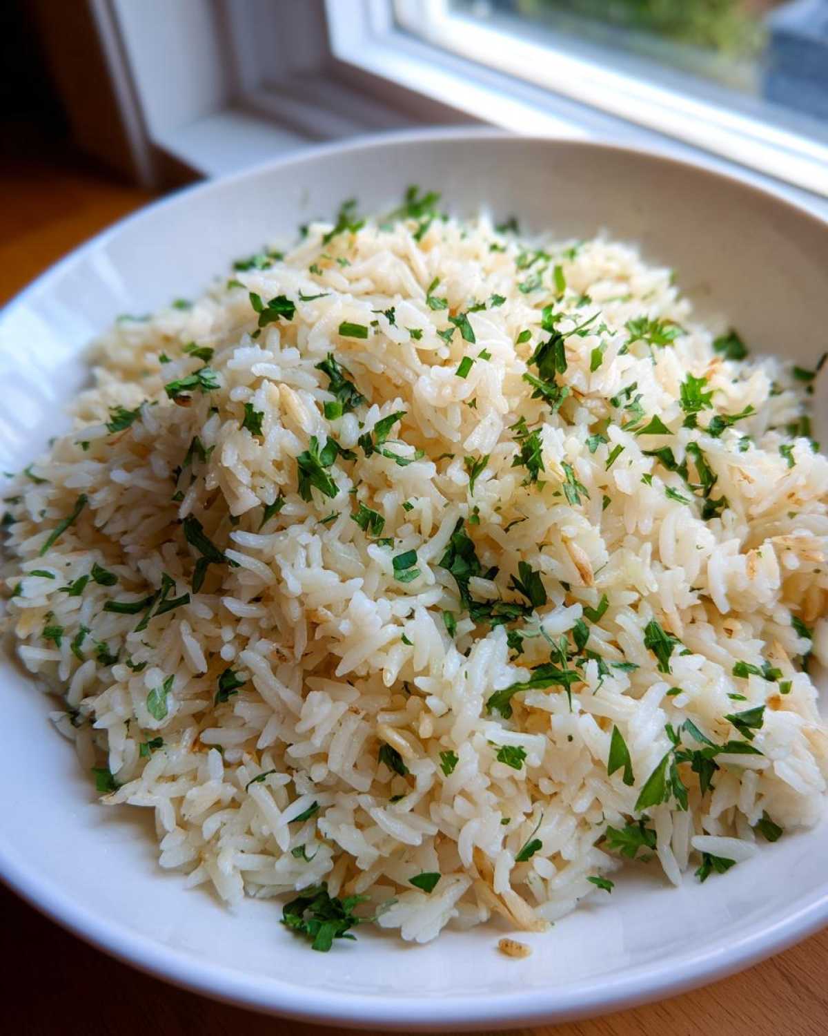 A close-up of fluffy rice pilaf served in a white bowl, topped generously with chopped green parsley.