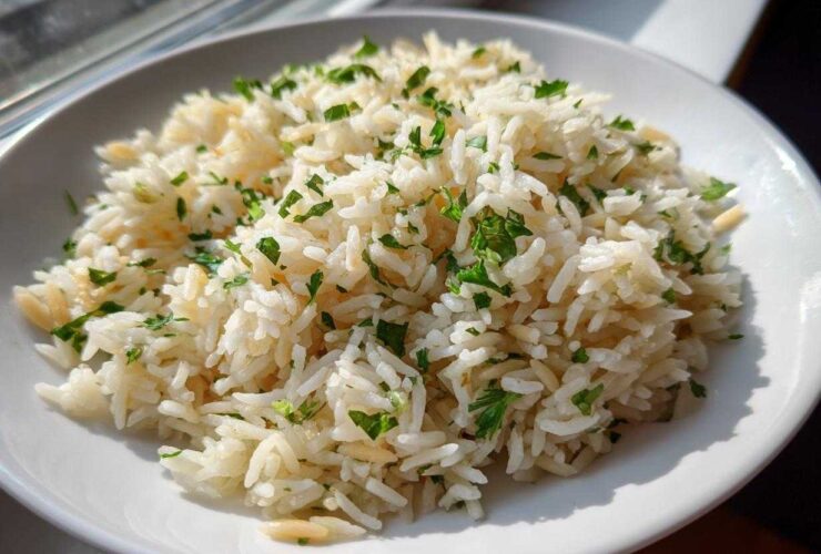 A close-up of fluffy rice pilaf garnished with fresh chopped parsley in a white bowl.