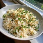 A close-up of fluffy rice pilaf mixed with toasted vermicelli and topped with fresh parsley.