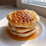 A stack of three fluffy sourdough discard pancakes glistening with maple syrup, showing many air pockets on top.