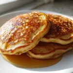 A stack of three golden-brown sourdough discard pancakes drizzled with maple syrup on a white plate.
