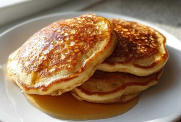 A stack of three golden-brown sourdough discard pancakes drizzled with maple syrup on a white plate.