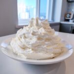 A large, fluffy mound of perfectly piped vanilla buttercream frosting sitting on a white plate.