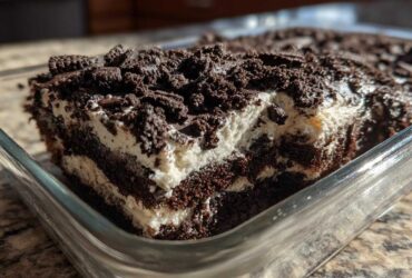 Close-up of a rich, layered slice of dirt cake featuring dark chocolate cake, white cream filling, and crushed cookie topping.