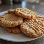A stack of golden brown peanut butter cookies with classic crisscross fork marks piled on a white plate.