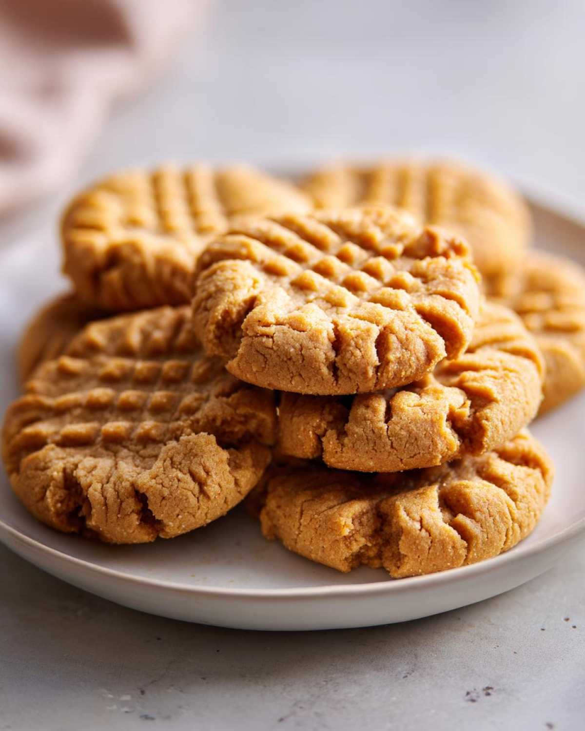 A close-up stack of freshly baked peanut butter cookies showing the classic crisscross fork marks.