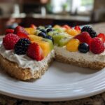 A slice removed from a fruit pizza sugar cookie topped with cream cheese frosting and fresh berries and kiwi.