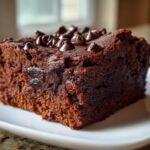 A close-up of a rich, fudgy slice of sweet potato brownies topped with chocolate chips on a white plate.