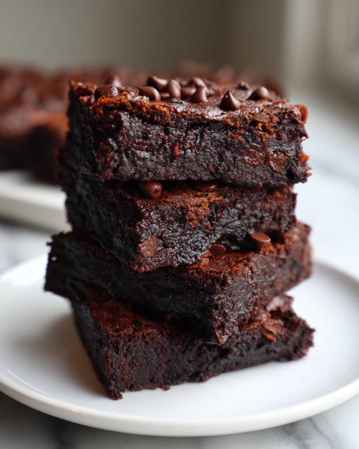 A stack of four fudgy sweet potato brownies topped with chocolate chips, sitting on a white plate.
