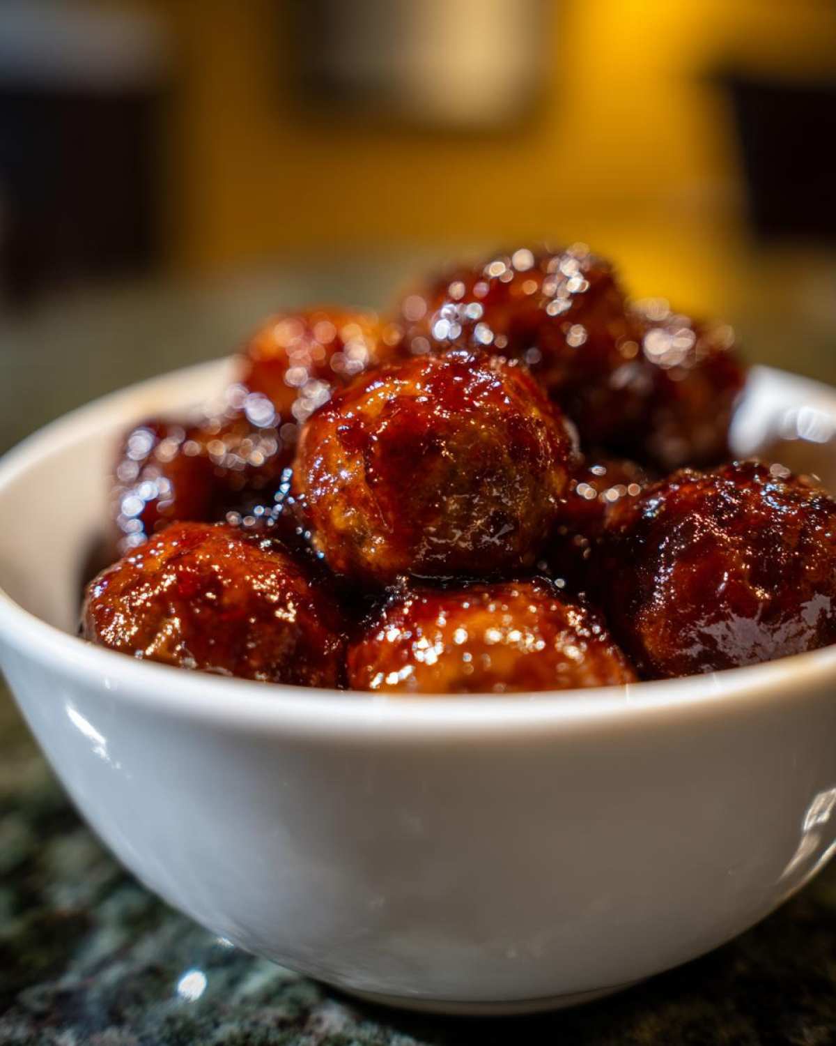 Close-up of shiny, glazed grape jelly meatballs piled high in a small white serving bowl.