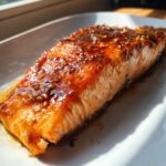 Close-up of a perfectly cooked salmon fillet glazed with a rich, shiny sauce and sprinkled with sesame seeds.