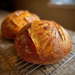 Close-up of a perfectly baked, round loaf of golden brown french bread cooling on a wire rack.