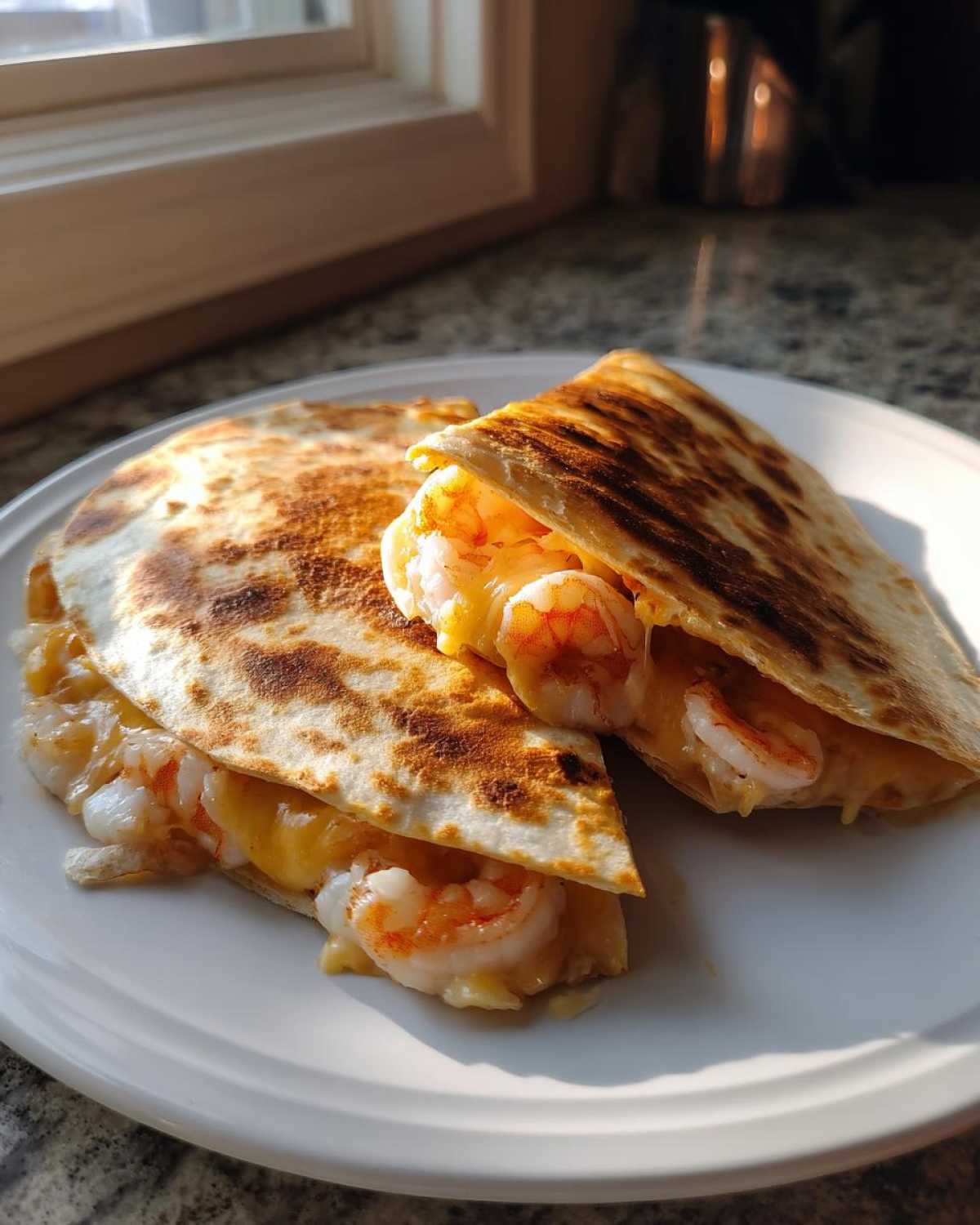 Two halves of a golden brown shrimp quesadilla, filled with melted cheese and plump shrimp, resting on a white plate.