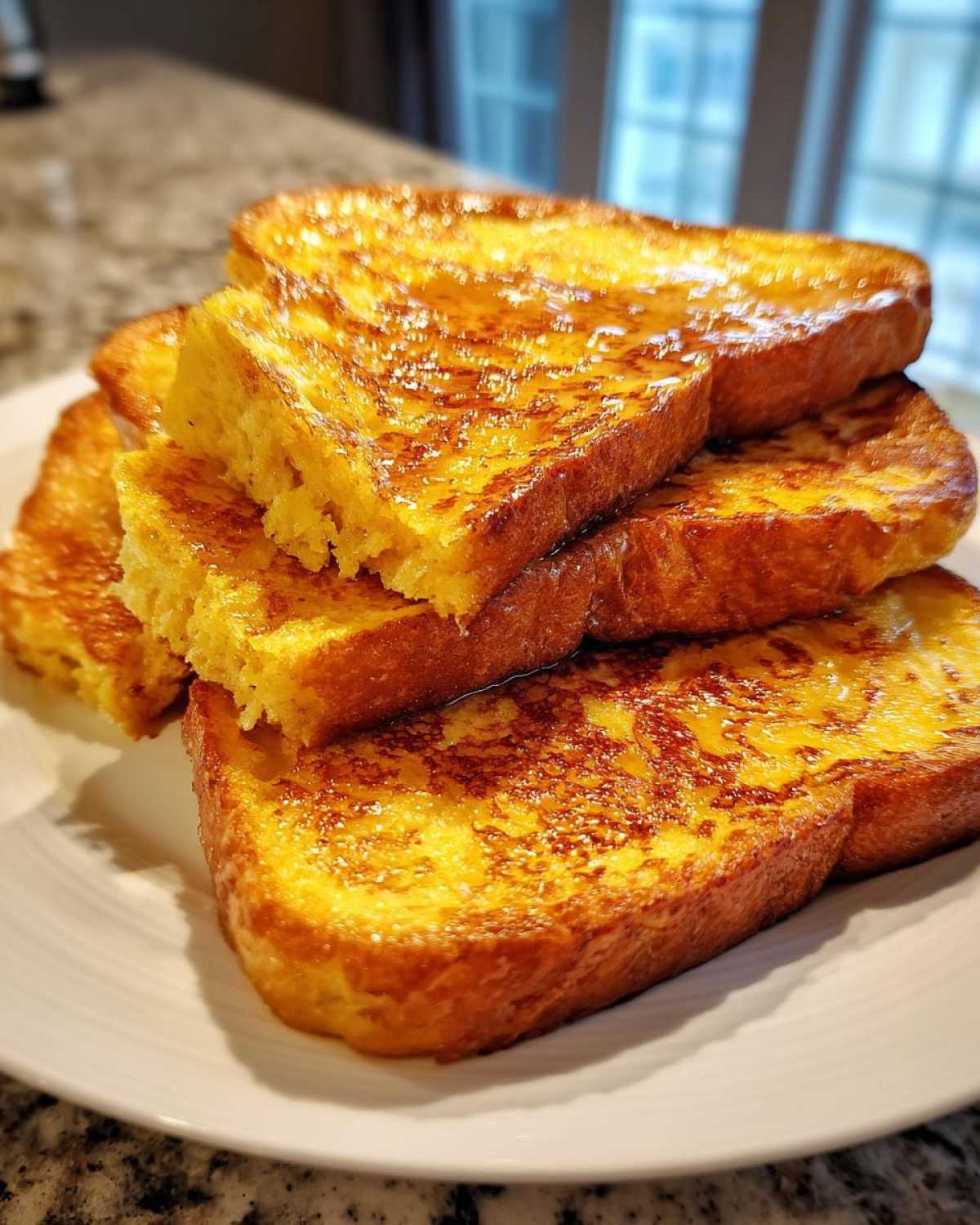A close-up of a stack of thick, golden brown french toast slices drizzled generously with syrup.