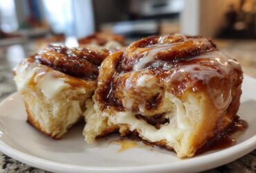 Two soft, gooey cinnamon rolls covered in caramel glaze and white frosting, one pulled apart to show the filling.