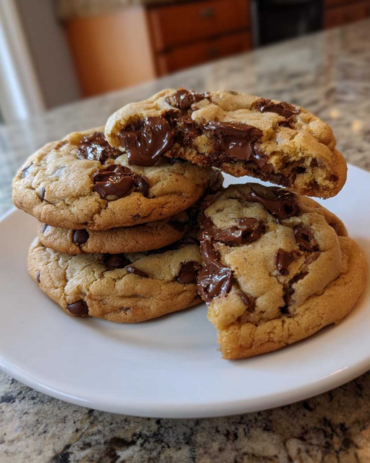 A stack of gooey homemade chocolate chip cookies with one broken open to show melted chocolate centers.