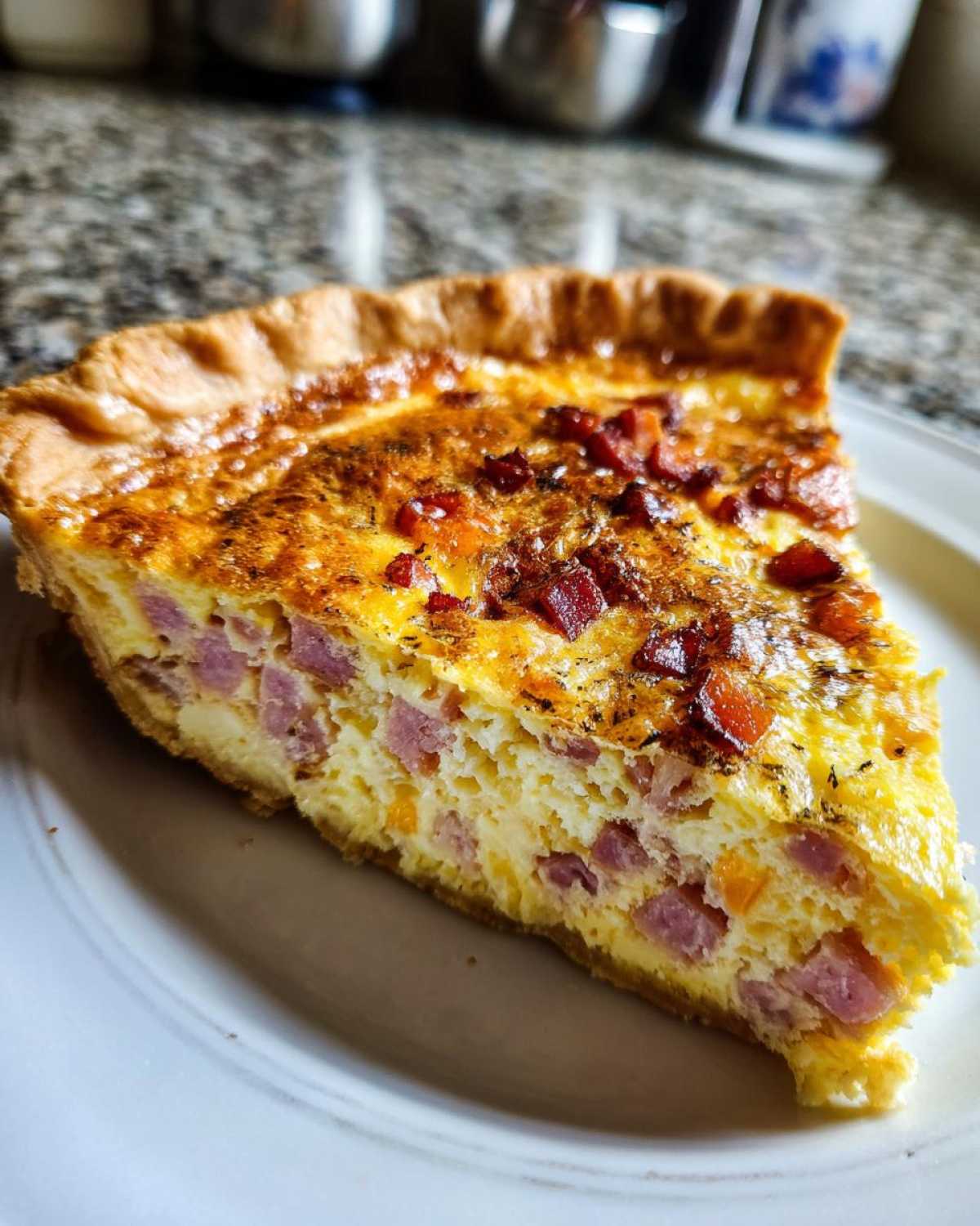 Close-up of a thick slice of ham and cheese quiche showing diced ham and a golden, cheesy top.