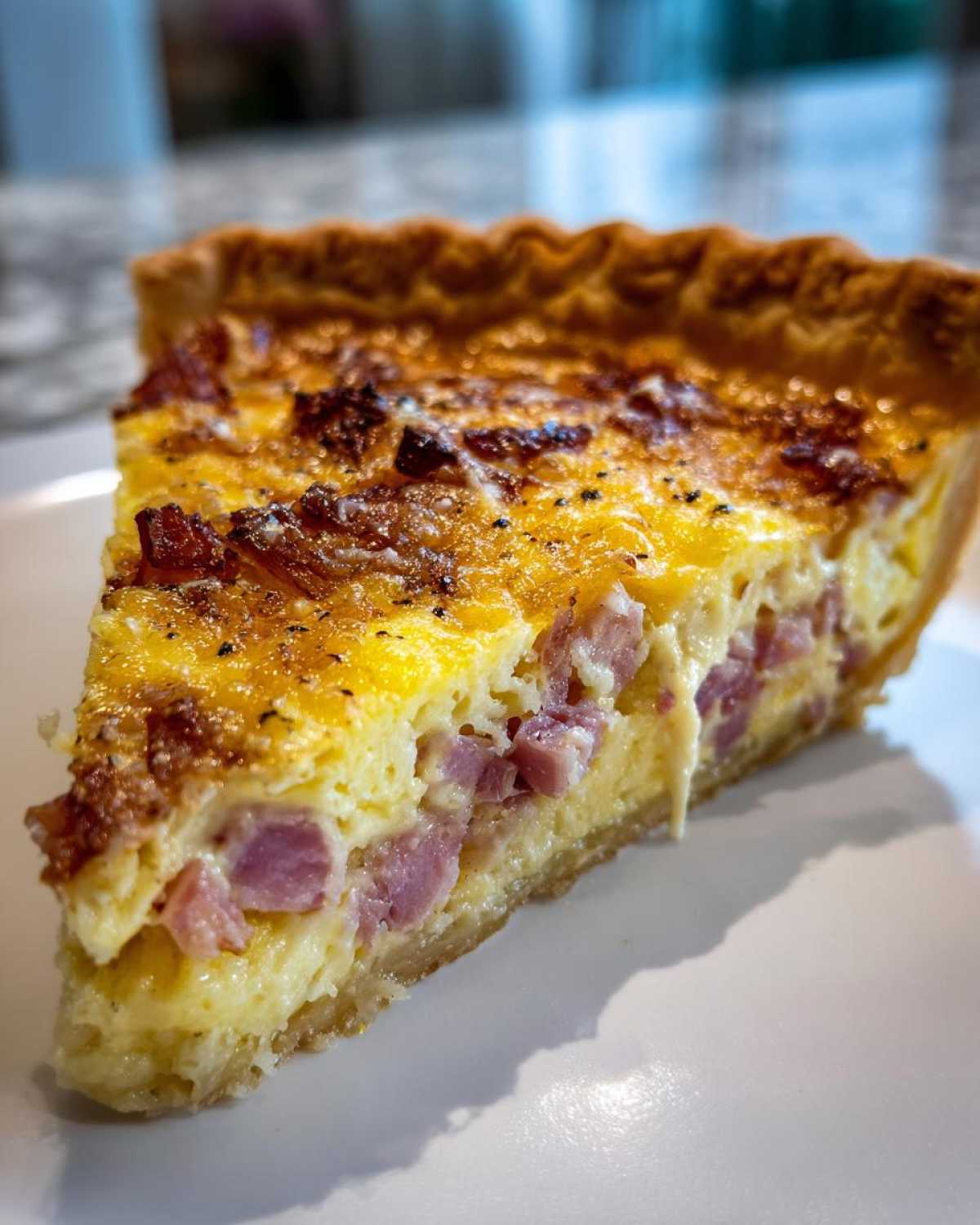 Close-up of a thick slice of Ham and Cheese Quiche showing the eggy filling and chunks of ham.