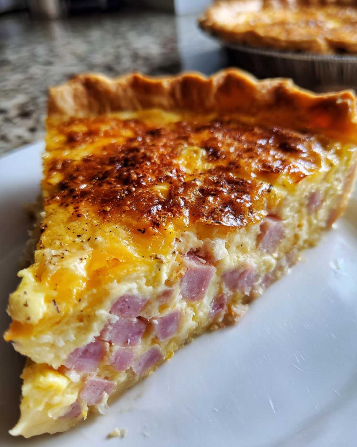Close-up of a thick slice of ham and cheese quiche showing diced ham in the creamy egg filling.