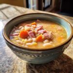 A close-up of a hearty bowl of Ham and bean soup, featuring white beans, diced ham, and sliced carrots.